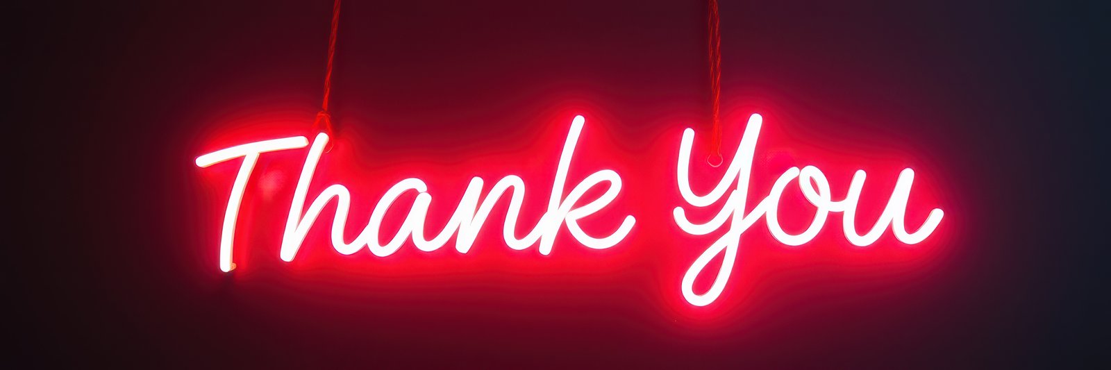 Bright red neon sign with the words thank you glowing against a dark background at a modern venue